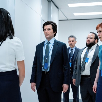 Mark S. (Adam Scott), Irving B. (John Turturro), Dylan G. (Zach Cherry), and Helly R. (Britt Lower) look at Miss Huang (Sarah Bock) in Severance season 2.