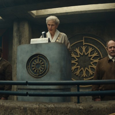 David Oyelowo and Will Patton stand near a podium while Geraldine James delivers a speech in Silo