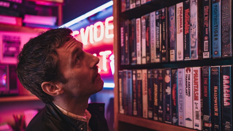 A man looking at a shelf of VHS horror tapes